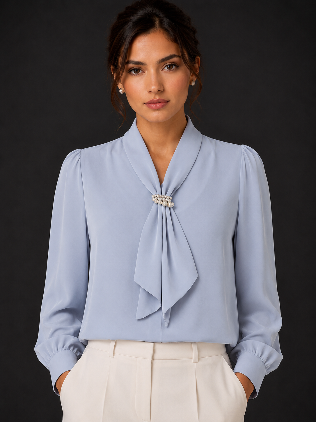 Woman wearing a light blue blouse with a tie detail against a dark background