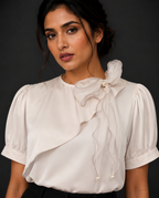 Woman wearing a white blouse with ruffled details against a dark background