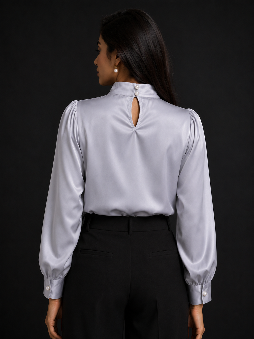 Woman wearing a light gray blouse with long sleeves and a cutout back design on a black background.