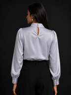 Woman wearing a light gray blouse with long sleeves and a cutout back design on a black background.