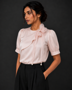 Woman wearing a light pink blouse with ruffled sleeves and a bow against a dark background