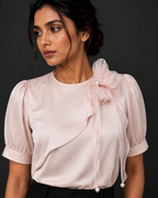 Woman wearing a light pink blouse with a bow detail on a dark background
