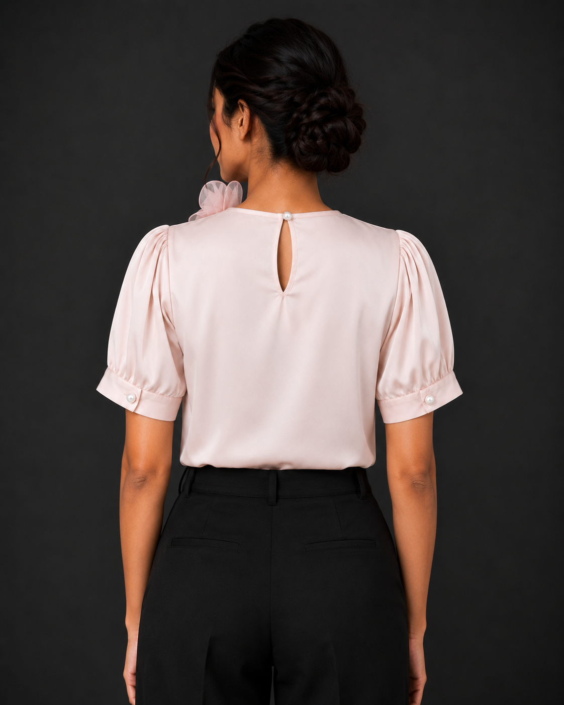 Woman wearing a light pink blouse with puffed sleeves and black pants against a dark background