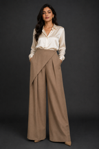 Woman wearing a white blouse and beige wide-leg pants against a dark background