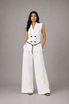 Woman wearing a white sleeveless blazer and wide-leg pants on a gray background