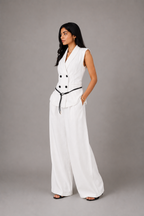 Woman wearing a white sleeveless vest and wide-leg pants against a gray background