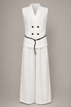White sleeveless jumpsuit with black buttons and belt on a beige background