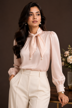 Woman wearing a light pink blouse with a bow tie and white pants against a dark background