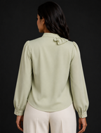 Woman wearing a light green blouse with long sleeves and a dark background