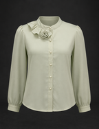 Light green blouse with ruffled collar and floral embellishment on a black background