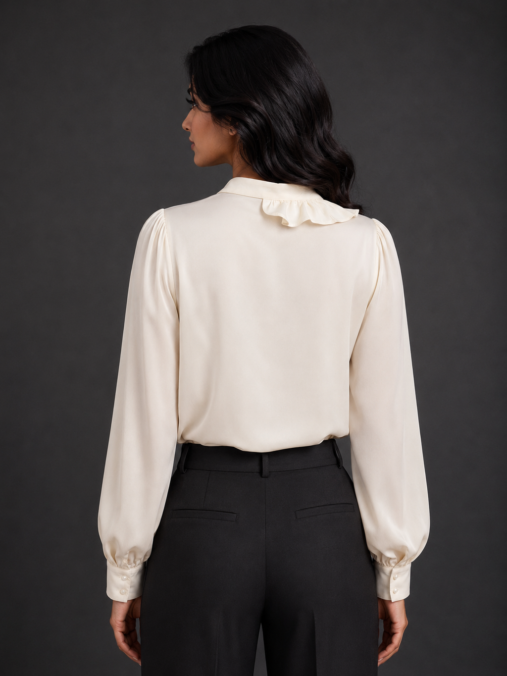 Woman wearing a cream blouse with long sleeves and black pants against a gray background