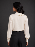 Woman wearing a cream blouse with long sleeves and black pants against a gray background