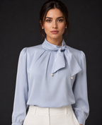 Woman wearing a light blue blouse with a bow tie against a dark background