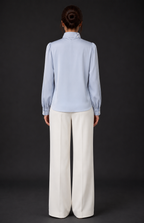 Person wearing a light blue shirt and white pants against a black background