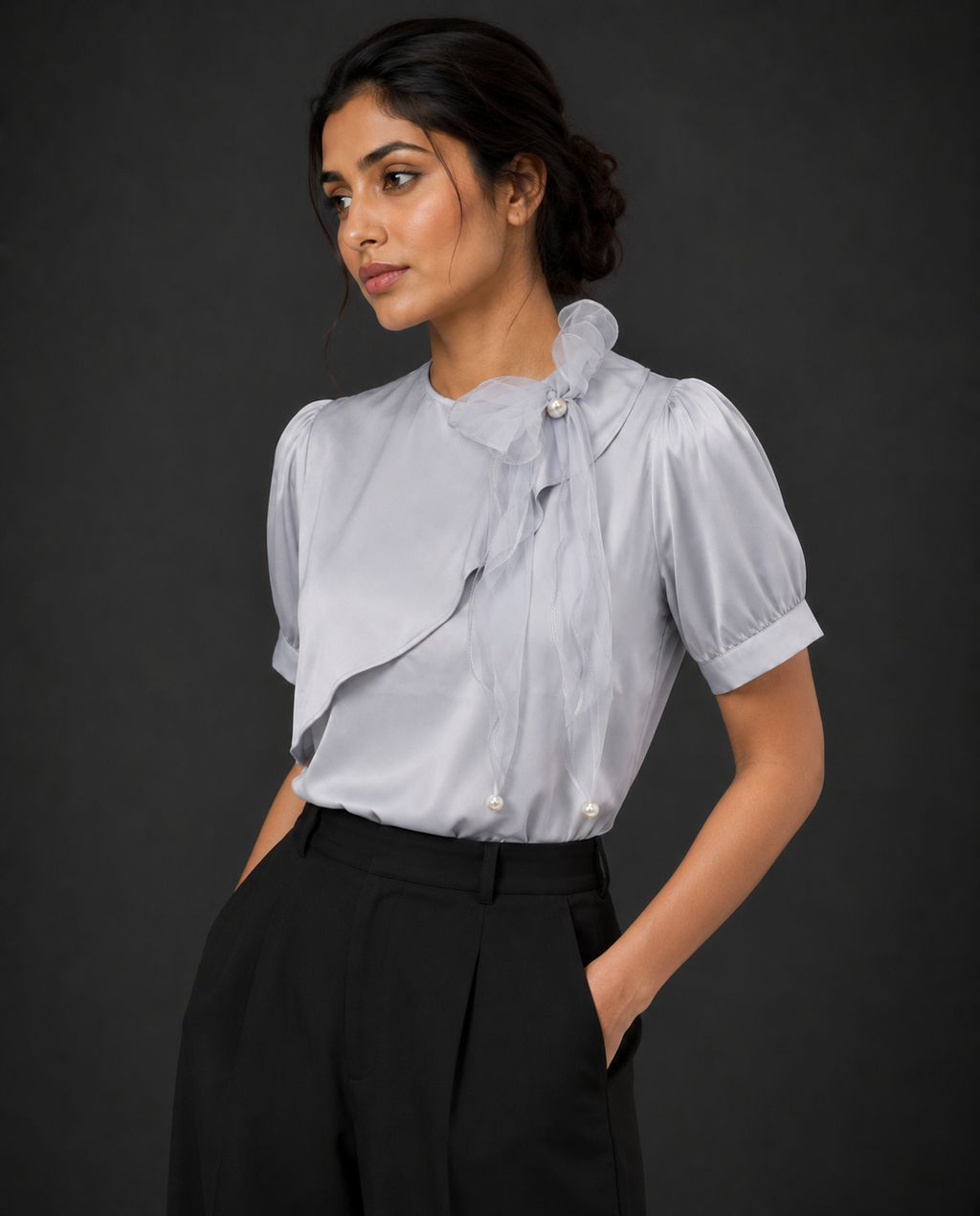 Woman wearing a light blue blouse with ruffled details and black pants against a dark background