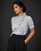 Woman wearing a light blue blouse with ruffled details and black pants against a dark background