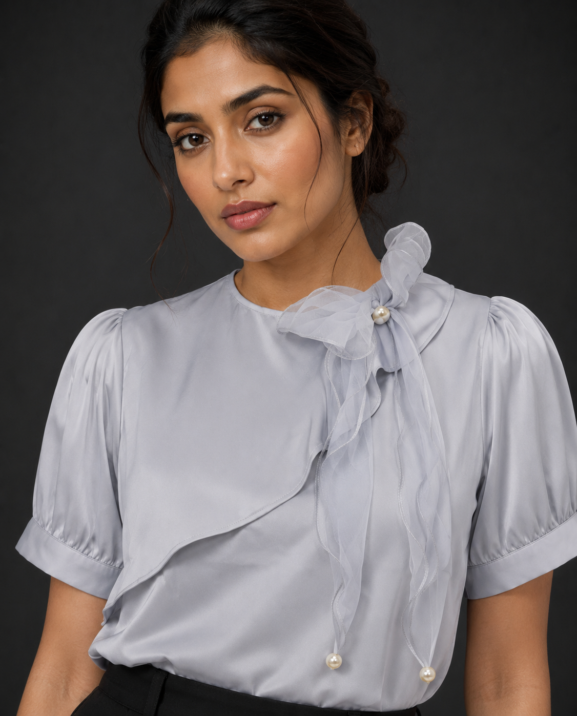 Woman wearing a light gray blouse with a bow detail on a dark background