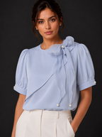 Woman wearing a light blue blouse with puff sleeves and pearl accents on a black background