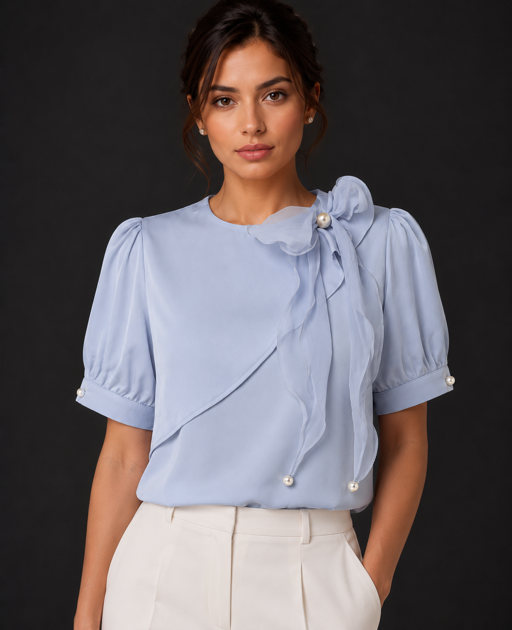 Woman wearing a light blue blouse with pearl details against a dark background