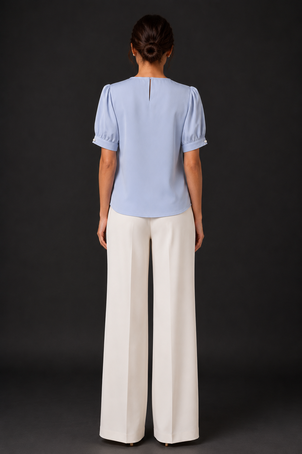 Person wearing a light blue top and white pants against a dark background