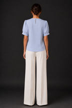 Person wearing a light blue top and white pants against a dark background