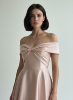 Woman wearing a light pink off-shoulder dress against a plain background