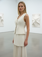 Woman wearing a cream-colored sleeveless top and pleated skirt in an art gallery setting.