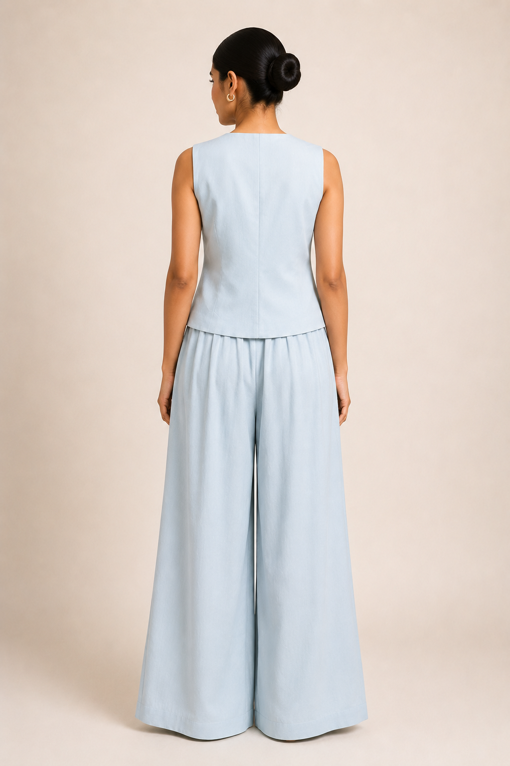 Woman wearing a light blue sleeveless top and wide-leg pants on a beige background