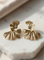 Gold leaf-shaped earrings on a marble surface