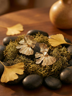 Gold leaf-shaped earrings on a bed of moss and stones with a blurred background