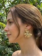 Woman wearing gold earrings with a green leafy background
