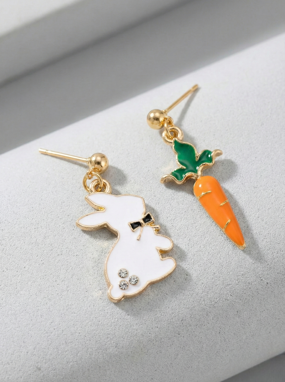 Pair of earrings with a rabbit and carrot design on a light gray background