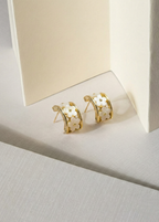Gold hoop earrings with cut-out design on a light background