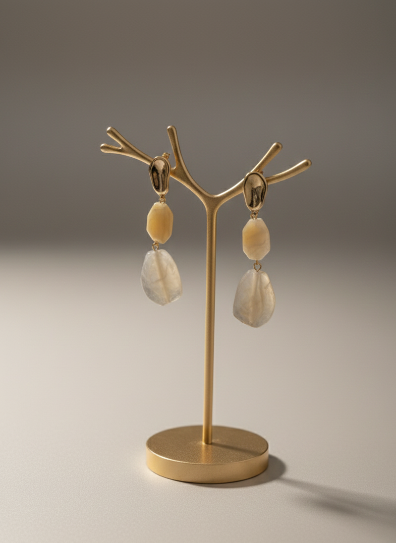 Gold earring stand with beige earrings on a gray background