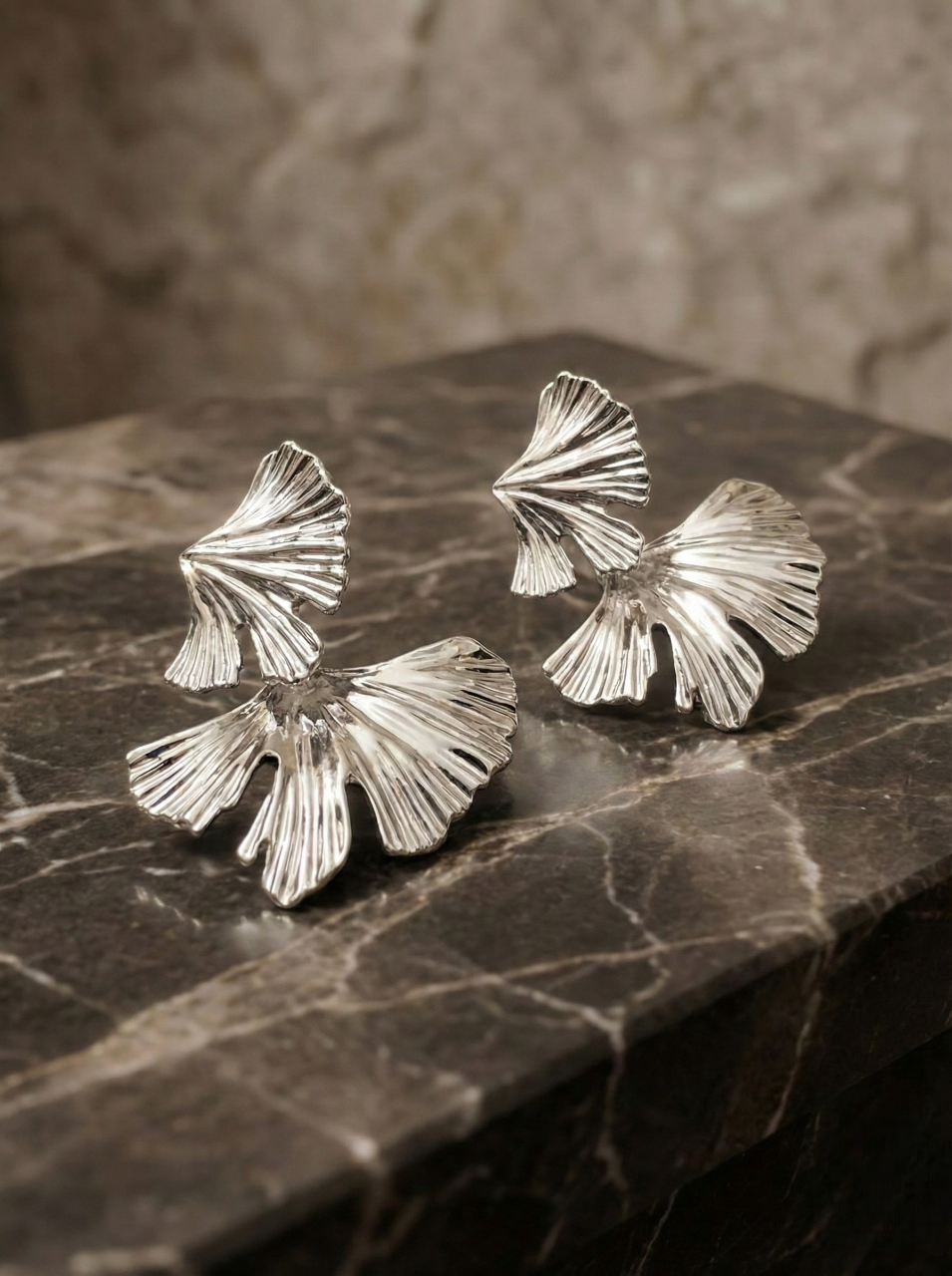 Silver leaf-shaped earrings on a dark stone surface