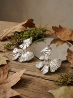 Silver leaf-shaped earrings on a wooden surface with leaves and moss.