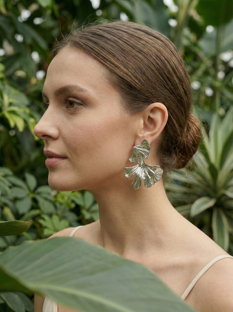Woman wearing silver leaf earrings with a green foliage background