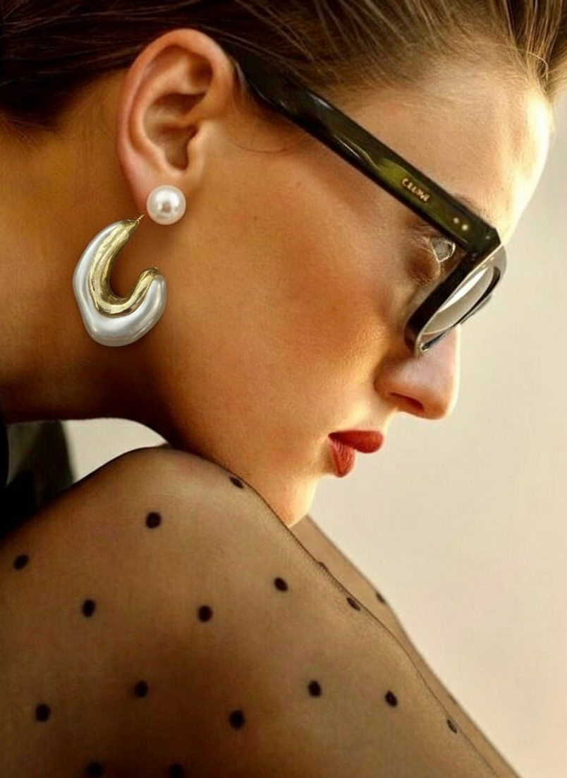 Close-up of a woman wearing large hoop earrings and glasses with a neutral background
