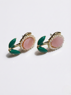 Pair of earrings with pink center, green leaves, and gold accents on a white background