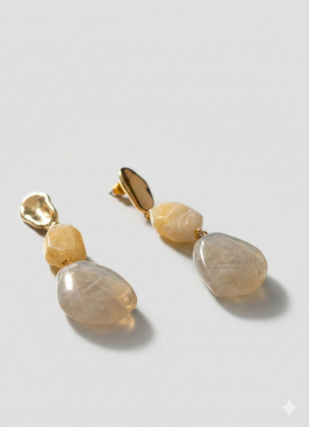 Pair of earrings with gold and stone components on a light gray background