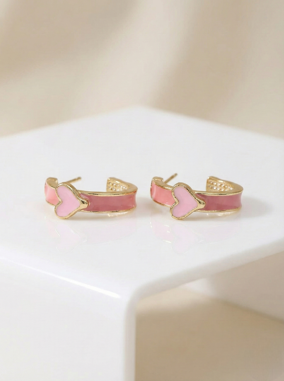 Pair of pink and gold hoop earrings on a white surface with a beige background
