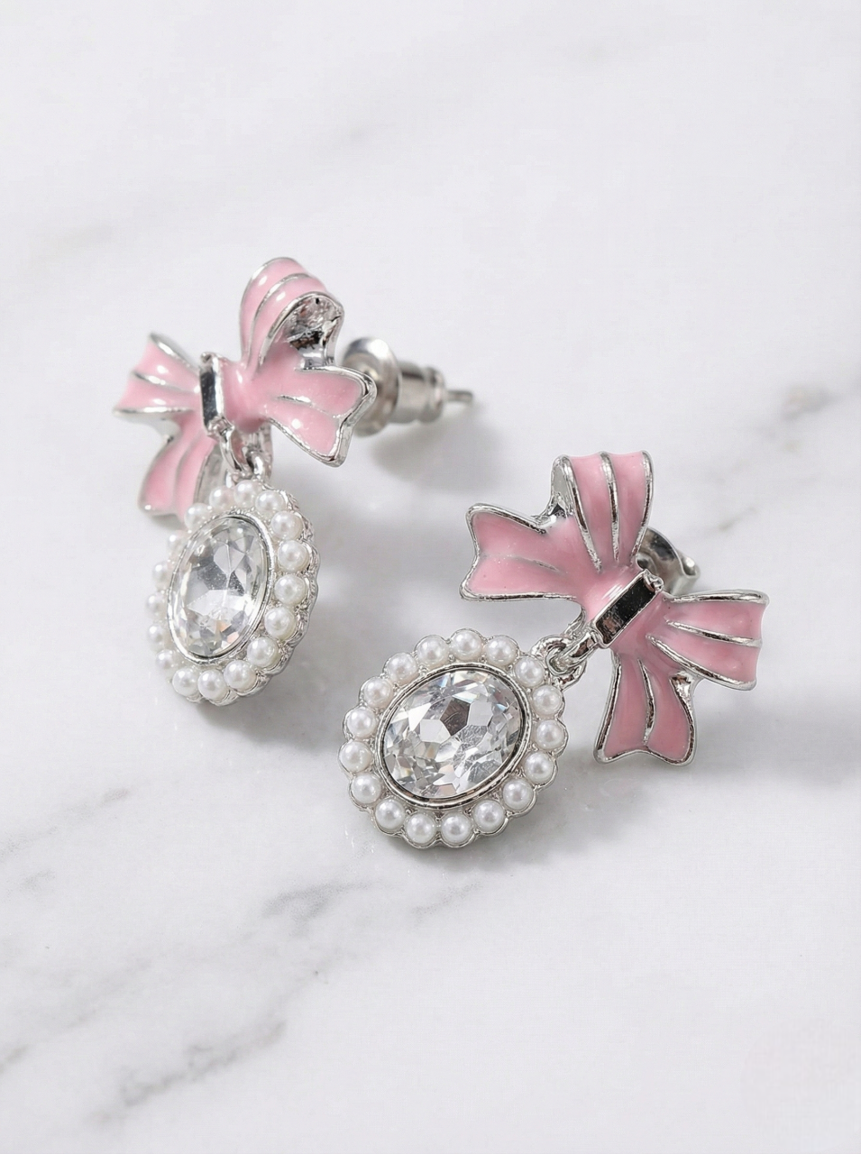 Pair of earrings with pink bows and clear crystals on a marble background