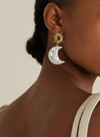 Close-up of a person wearing gold and silver earrings against a neutral background