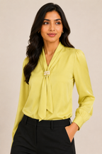Woman wearing a light green blouse with a tie detail against a beige background