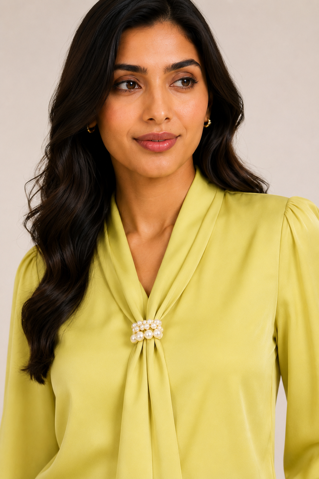 Woman wearing a light green blouse with a pearl detail on a neutral background
