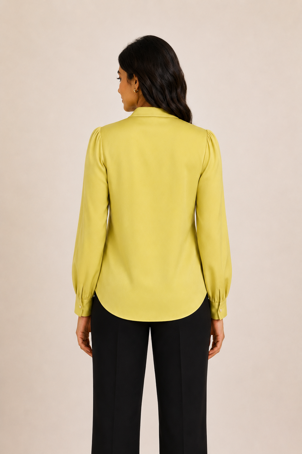 Person wearing a light green blouse and black pants against a beige background