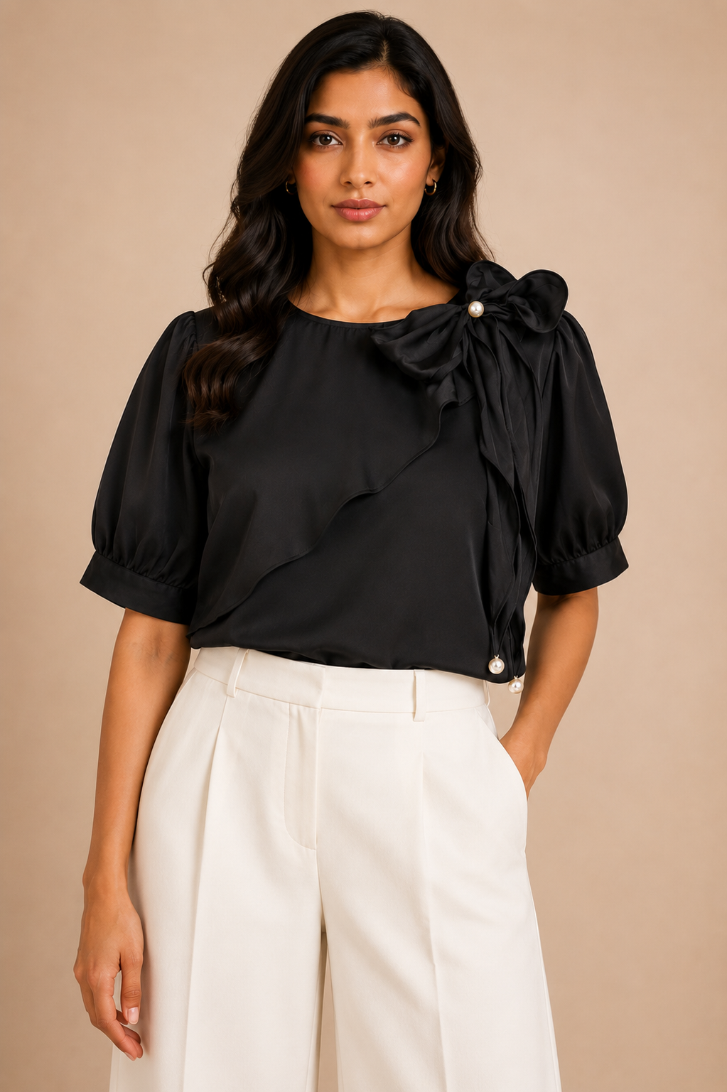 Woman wearing a black blouse with ruffled details and white pants against a beige background