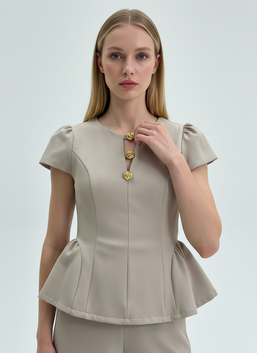 Woman wearing a beige peplum top with gold buttons on a light gray background