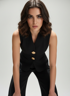 Woman wearing a black sleeveless blazer with gold buttons on a gray background