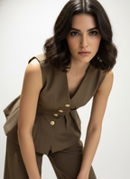 Woman wearing a brown sleeveless top with gold buttons on a white background